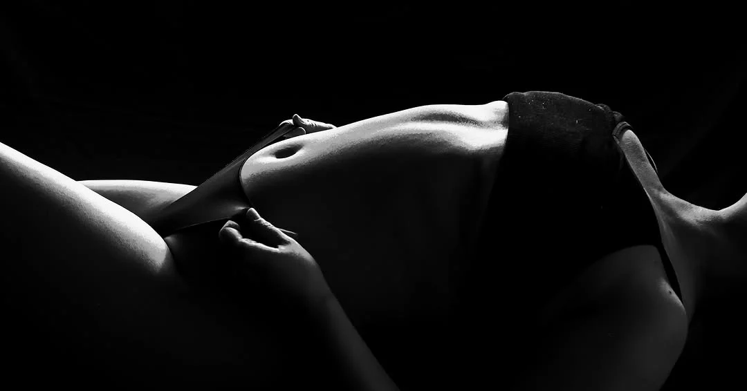 A black and white study of a reclining figure, lit from the side against a dark background